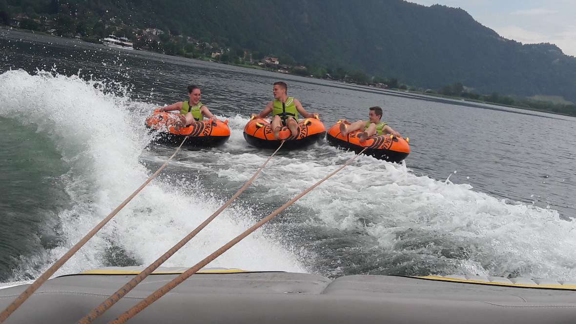 Schüler sitzen im Reifen und werden hinter einem Boot hergezogen am See